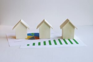 Three small wooden house models placed on top of printed property data charts, including a pie chart and a bar graph, against a white background